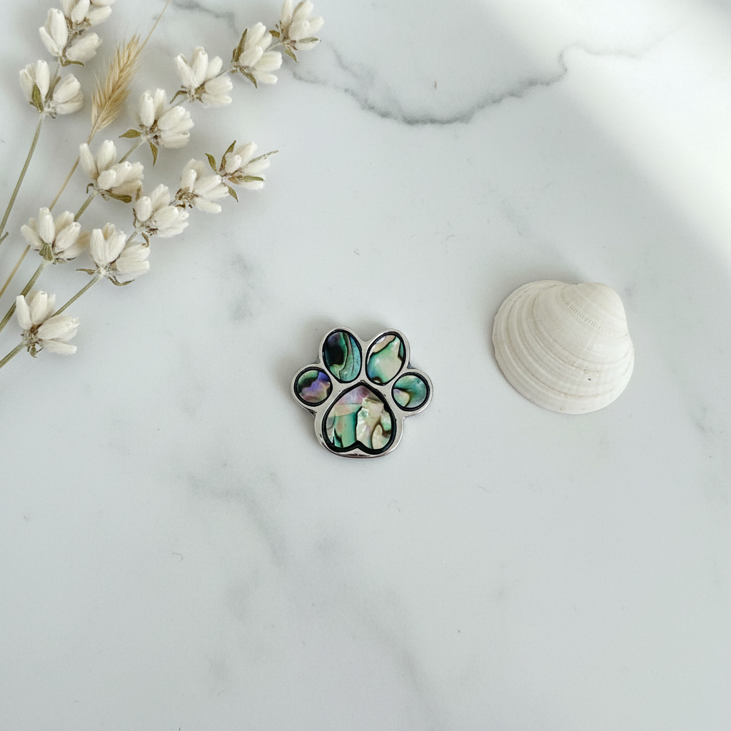 Paua shell paw print pin badge lifestyle flat lay on white marble